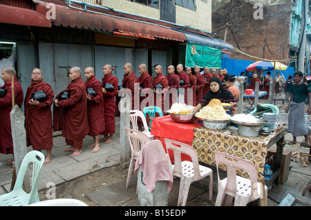 Buddhist monks pass a food stall on their way to their morning alms walk in the center of Yangon Myanmar, Burma Stock Photo