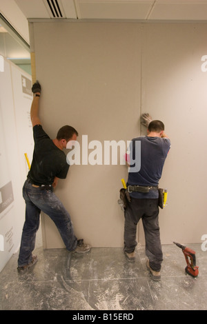 Two workmen install a plasterboard partition in a newly constructed office building. Stock Photo