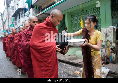 A woman serving Buddhist monks rice on their morning alms walk in the city of Yangon Republic of the Union of Myanmar Stock Photo