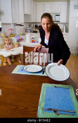 Still in her office clothes a professional woman hurries to set the dinner table for her family in Lake Forest CA Stock Photo