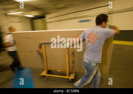 A pair of workmen move a sheets of plasterboard to the goods lift of an office block in London Stock Photo