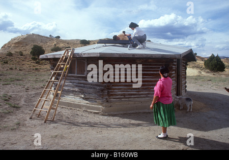 A Navajo woman watches as two college students install a solar panel on her hogan (house) in northern Arizona. Stock Photo