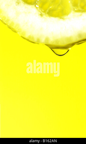 lemon juice dripping from a slice of lemon against a bright yellow background Stock Photo