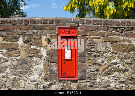 Horizontal close up of a bright red cast iron Victorian letter box on a stone wall on a sunny day. Stock Photo