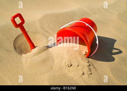 Horizontal view of a red plastic bucket and spade lying in the sand on the beach Stock Photo