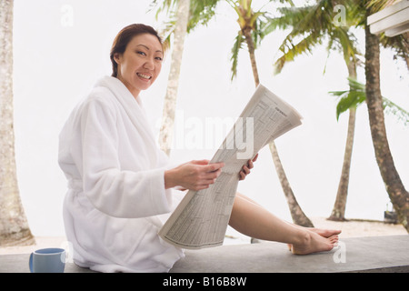 Asian woman in bathrobe reading newspaper