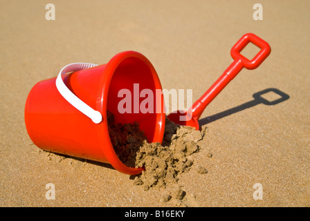 Horizontal view of a red plastic bucket and spade lying in the sand on the beach Stock Photo