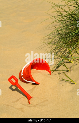 Vertical close up of a red plastic bucket and spade in the sand dunes on a sunny day Stock Photo