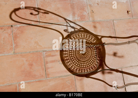 Strong shadow of classic French iron garden chair on tiled patio floor Stock Photo