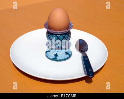 boiled egg in eggcup with teaspoon on white plate set on sunlight light brown table. Stock Photo
