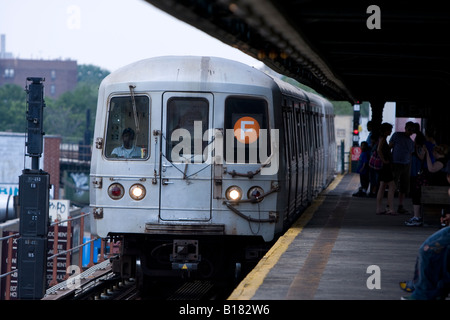 A Coney Island bound F train in Brooklyn NY stops at an elevated subway platform Stock Photo