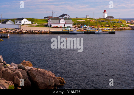 Boats docked in Neils Harbour with the Neils Harbour Lighthouse on Neils Harbour Point, Cabot Trail, Cape Breton, Nova Scotia, C Stock Photo