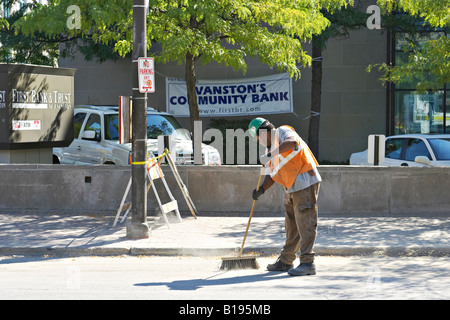 WORKERS Evanston Illinois Man sweep street in construction area using push broom wear hard hat orange safety vest Stock Photo
