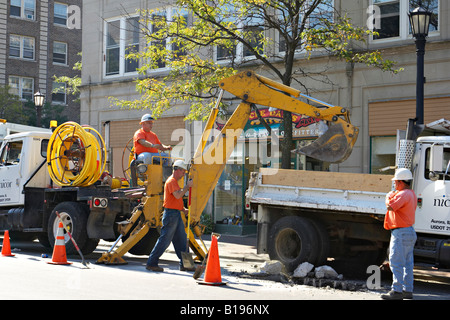 WORKERS Evanston Illinois Utility construction workers dig hole in asphalt street machinery lift pieces into back of truck Stock Photo