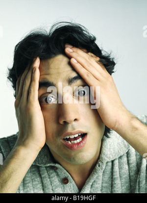 Young man holding head, raising eyebrows, staring at camera, portrait Stock Photo