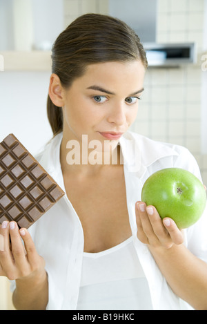 Young woman holding apple in one hand and large bar of chocolate in the other Stock Photo