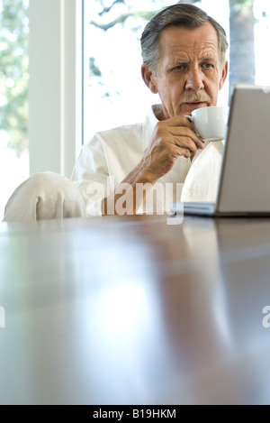 Senior man drinking coffee and using laptop Stock Photo