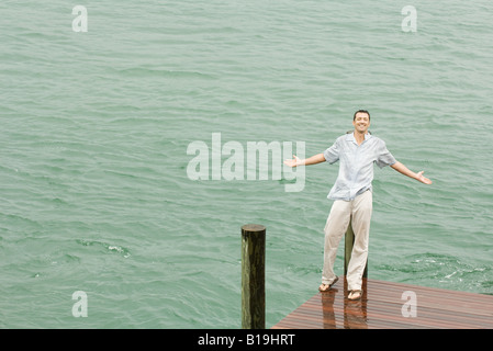 Man leaning against dock post, getting wet, arms out, smiling at camera Stock Photo