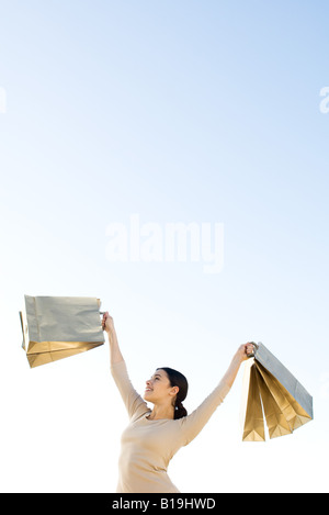 Woman holding up shopping bags, smiling, low angle view Stock Photo