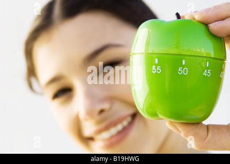 Woman holding up kitchen timer, smiling at camera, focus on foreground Stock Photo