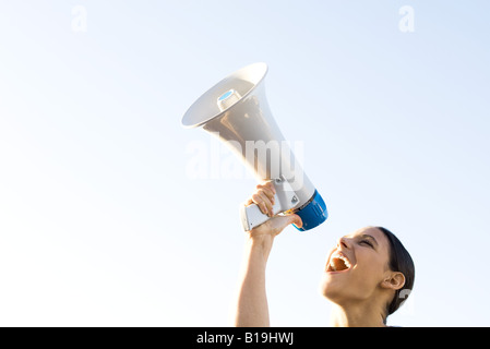 Woman shouting into megaphone, low angle view, cropped Stock Photo