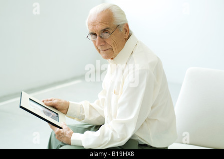 Senior man sitting, holding photograph, looking at camera Stock Photo