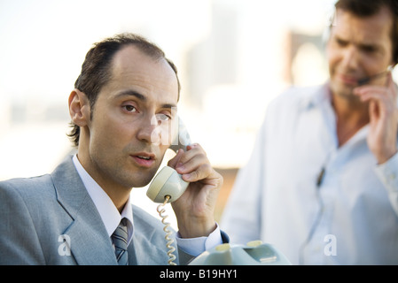 Businessman using landline phone, man in background using headset Stock Photo