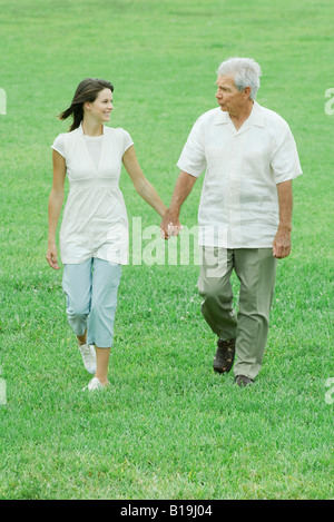 Grandfather and teen granddaughter walking outdoors, holding hands, smiling at each other Stock Photo
