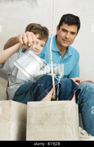 Father and son watering potted plant together, both smiling Stock Photo