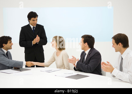 Business associates at conference table, two shaking hands, the others clapping Stock Photo