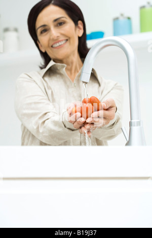 Woman rinsing Roma tomatoes under faucet, smiling at camera Stock Photo