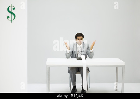 Man sitting at desk with adding machine, puffed cheeks, hands raised Stock Photo