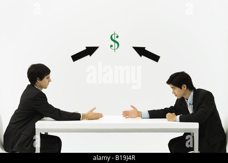 Two businessmen face to face, reaching to shake hands, dollar sign and arrows between them Stock Photo