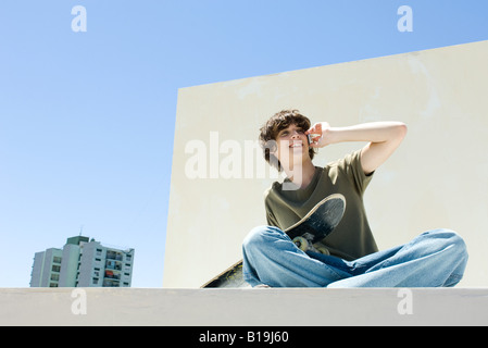 Teen boy using cell phone in urban setting, holding skateboard Stock Photo
