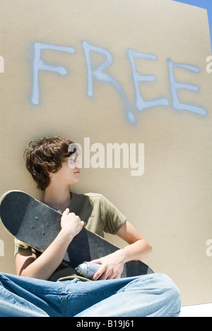 Teen boy holding skateboard and spray paint can, under the word 'free' on wall