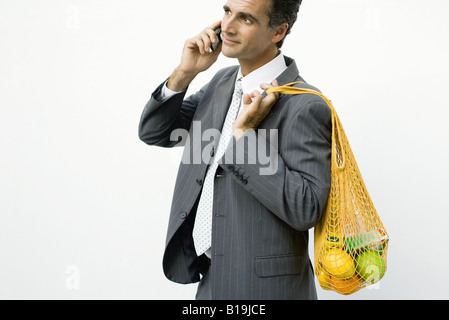 Businessman using cell phone, mesh bag of groceries slung over his shoulder Stock Photo