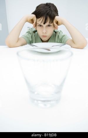 Boy sulking at kitchen table, leaning on elbows, empty glass in foreground Stock Photo