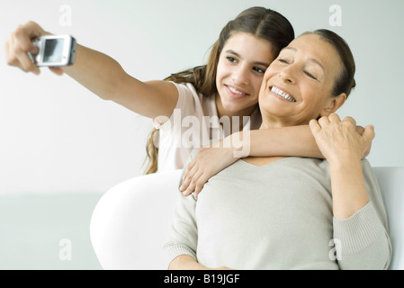 Teen girl photographing self and grandmother with photophone, both smiling Stock Photo