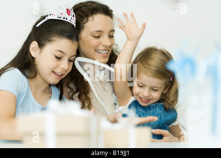 Mother and two daughters playing dress-up, smiling, one girl wearing tiara, the other wearing wings Stock Photo