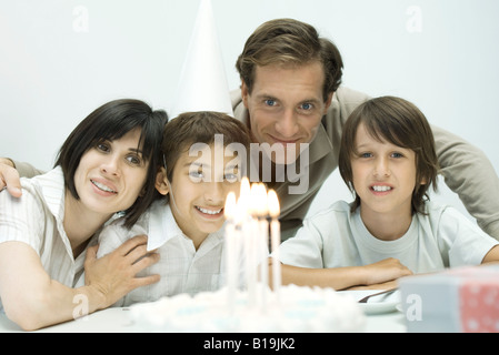 Family in front of birthday cake with lit candles, one boy wearing party hat Stock Photo