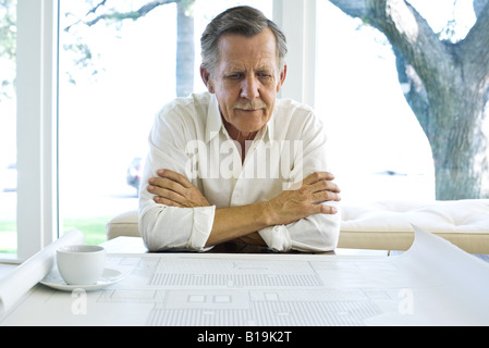 Man looking at blueprint, coffee cup nearby Stock Photo