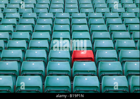 One red seat amongst rows of green seats in a sports stadium Stock Photo