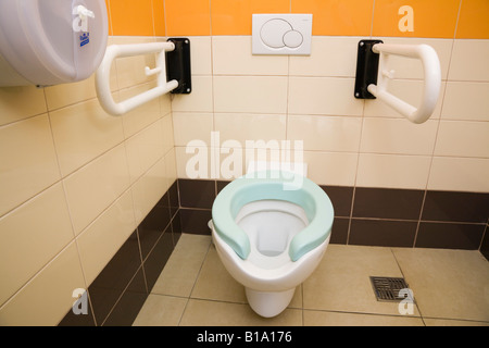 Public disabled toilet inside clean tiled cubicle with dual flush button on wall and drop down handrail supports Stock Photo