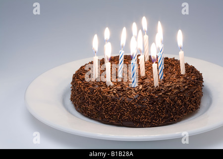 Chocolate Birthday Cake with lit candles on a white plate Stock Photo