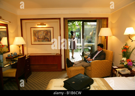 businessman using laptop and young woman drinking coffee in hotel room Stock Photo