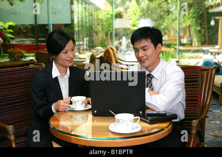 businessman and businesswoman drinking coffee and using laptop at hotel hall Stock Photo