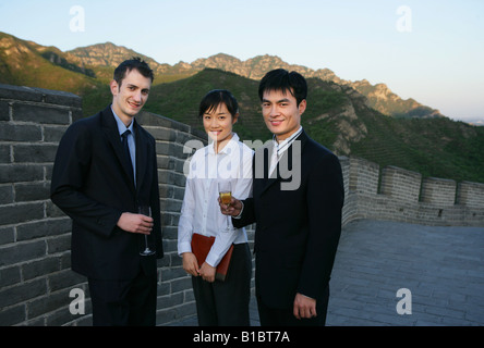two businessmen and one businesswoman standing and holding wineglasses and notebook on Great Wall,Beijing,China Stock Photo