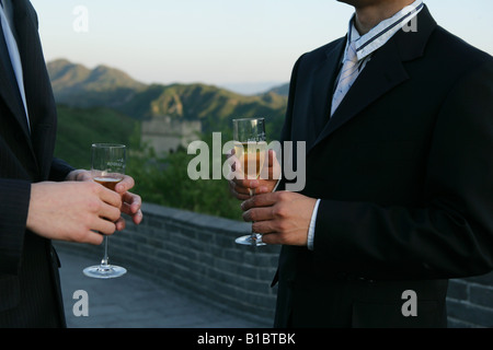 Chinese businessman and caucasian businessman holding wineglasses and handshaking on Great Wall,Beijing,China,close-up Stock Photo