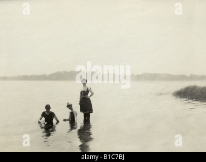 Antique photograph, circa 1890s, of two women and 1 man dressed in Victorian-era bathing suits swimming in a New England lake. Stock Photo