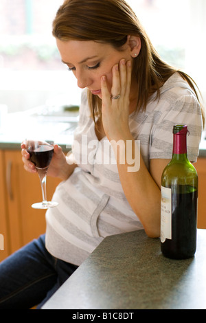 Worried looking pregnant woman drinking wine Stock Photo